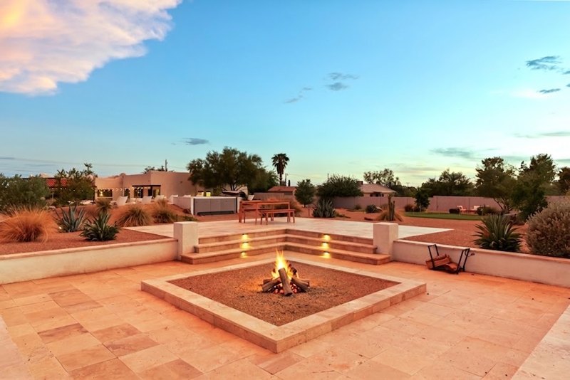 The sunken fire pit lit at dusk, with the house and the desert behind it